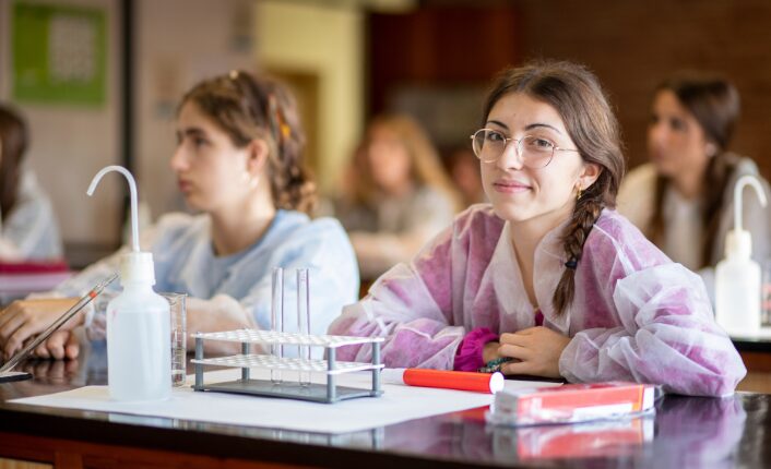 a woman in pink and white lab coats sitting at a table with a small object on it